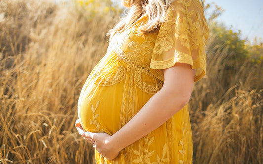Une femme enceinte vêtue d'une robe d'été jaune tient son ventre.